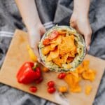Dłonie trzymające nachos z guacamole i pomidorkami na desce