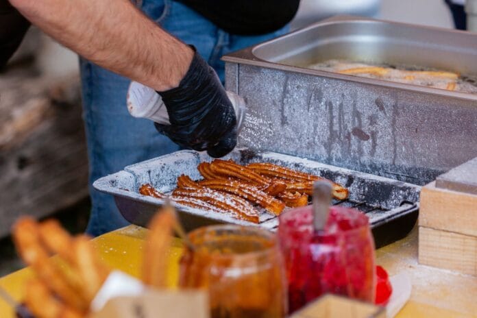 Zbliżenie na ulicznego sprzedawcę przygotowującego churros z dodatkami Zbliżenie na ulicznego sprzedawcę przygotowującego churros z dodatkami